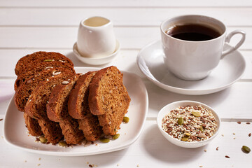 Wholegrain bread on a white plate and a cup of coffee on the table. Healthy breakfast.
