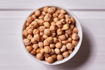 Chickpea seeds in a white bowl on a white wooden background.