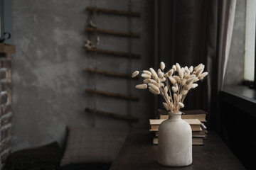 Retro bottle with rabbit tail grass bouquet, books on dark brown table. Minimal modern interior decoration concept.