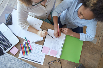 Top view of mixed race teen girl doing math task, school homework together with female teacher in the living room at home
