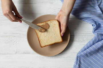Female hands spreading toast bread with peanut butter, making healthy breakfast, top view
