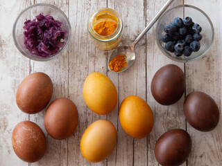Colorful Easter eggs with their natural dyes of beets curcuma and blueberries on wooden surface