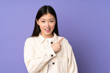 Young asian woman isolated on purple background pointing to the side to present a product
