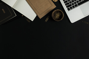 Black background office workspace desk with laptop computer, craft notebook sheet. Flat lay, top view minimalist aesthetic work, business composition.