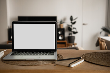 Fototapeta premium Laptop computer with blank screen, notebooks on wooden table in warm sunlight room. Aesthetic minimal interior design template with mockup copy space. Blog, web, social media concept.