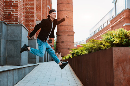 stylish young man in jeans and a cap makes a jump in the city as if he is running through the air. Cheerful active youth of a man.