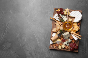 Cheese plate with honey, grapes and nuts on grey table, top view. Space for text