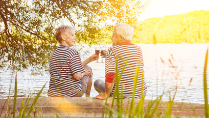 Elderly couple of seniors drinking red wine by the lake