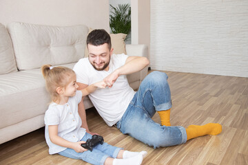 father spend time with little daughter, family sit on floor competing in video games, weekend activity, free time concept.