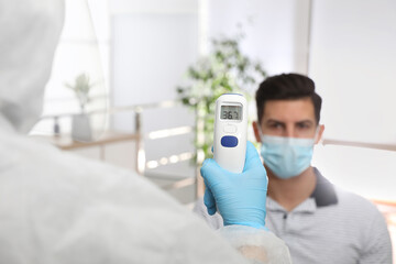 Doctor measuring man's temperature in office, closeup. Prevent spreading of Covid-19