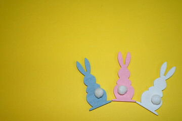 Fototapeta na wymiar three wooden figurines of a blue, pink and white Easter bunny with white tails lie on a yellow background, top view. Easter holiday