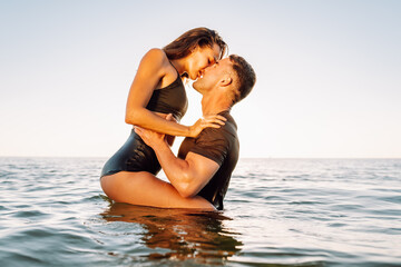 Happy young fit couple embrace each other with love in the sea or ocean at summer sunset. Romantic...