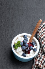 Cottage cheese with blueberry jam in ceramic bowl on black stone background