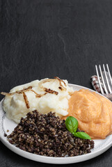 Traditional Scottish haggis with neeps and tatties on black stone background