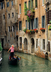 Fototapeta na wymiar Gondola and Gondolier and flower-filled window boxes on side canal in Venice