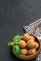 Mini scotch eggs in wooden bowl on black stone background