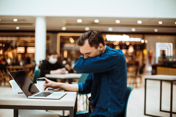 man sneezes sitting at a table in a cafe