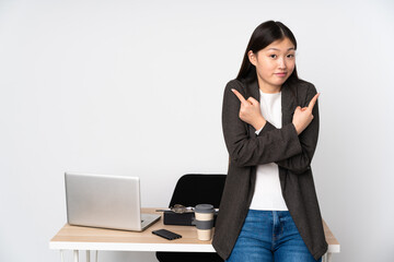 Business asian woman in her workplace isolated on white background pointing to the laterals having doubts