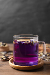 Glass mug of organic blue Anchan on wooden table, space for text. Herbal tea