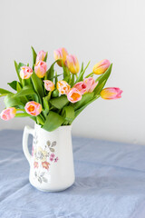 Beautiful spring bouquet of pink tulips in a jug on the table, flowers in a home interior