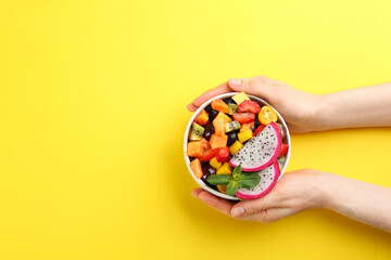 Woman with bowl of delicious exotic fruit salad on yellow background, top view. Space for text