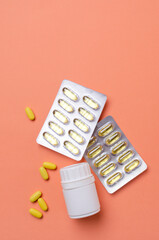Top view of white bottle of vitamin c, blisters of fish oil capsules on the orange surface
