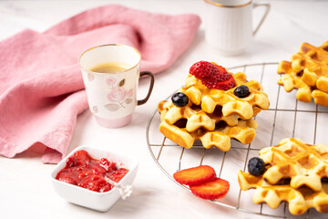 Delicious breakfast table, waffles with berries, jam and cup of coffee.
