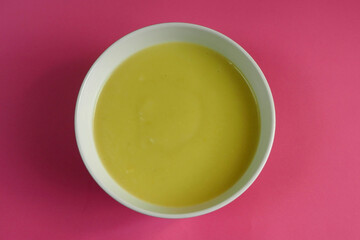 white plate with cream soup of zucchini, potatoes, cream, onions on a pink background top view . cooking gluten-free food at home