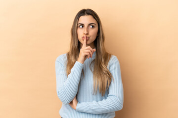 Young caucasian woman isolated on beige background showing a sign of silence gesture putting finger in mouth