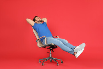 Young man relaxing in comfortable office chair on red background
