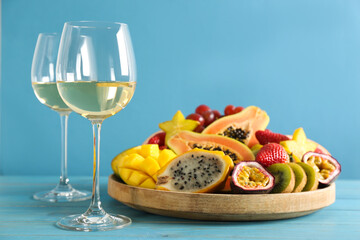 Delicious exotic fruits and glasses of wine on light blue wooden table