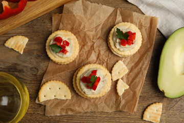 Delicious crackers with humus, bell pepper and parsley on wooden table, flat lay