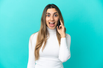 Young caucasian woman using mobile phone isolated on blue background with surprise facial expression