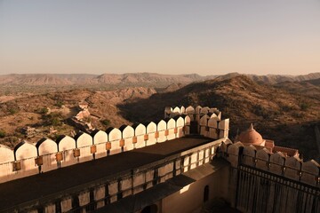Looking from the battlement studded ramparts of Kumbhalgarh Fort, India, towards the arid Aravalli hill range, some Jain and Hindu temples to the left and a dusty yellowish desert sky in the distance