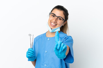 Young woman dentist holding tools isolated on white background showing and lifting a finger