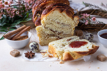 Cinnamon babka or swirl brioche bread with jam. Easter background with quail eggs, flowers and handmade wreath of twigs. Cinnamon roll bread.