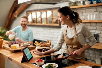 Happy woman using digital tablet while preparing food in the kitchen.