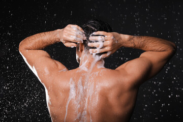 Obraz na płótnie Canvas Man washing hair while taking shower on black background