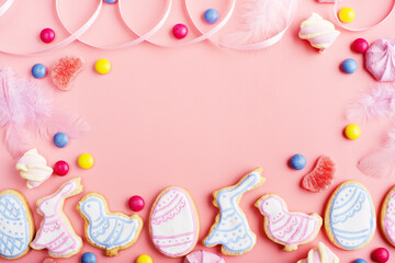 Candies and Easter frosted cookies in shape of egg chicken and rabbit on pink background. Flat lay mockup with copy space.