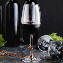 Wine glass with red wine. Wine composition on black stone table square. Red Wine bottles, grape...