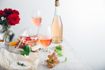 Rose wine in different wineglasses, bottle on white table with grapes cheese, snacks bouquet of flowers. modern still life Rose Wine composition on light grey concrete background with copy space