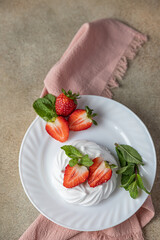Mini Pavlova meringue cakes with strawberries and mint on a plate, concrete background. Top view.