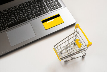 Laptop, shopping trolley, yellow credit card on a white background. Concept for online shopping,...