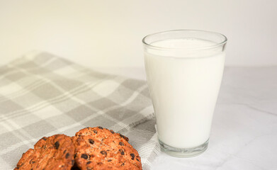 A glass of milk, chocolate oatmeal cookies and crumbs on a white plate in the rays of the sun. Tasty breakfast. The concept of proper nutrition and weight loss. copy space for text