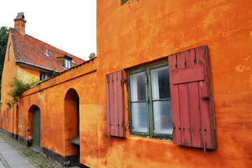Old medieval district in Copenhagen, Denmark. Orange facade of the house of Nyboder district, window with shutters on the foreground.