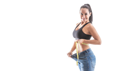 Fit good-looking woman shows great weight loss by loose jeans wearing sports bra on an isolated white background