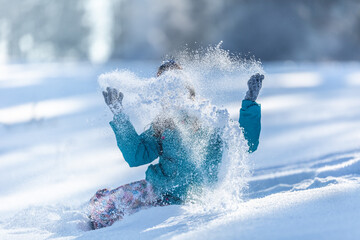 Child throwing powder snow into the air sitting on fresh snow on the ground