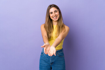 Young woman over isolated purple background holding copyspace imaginary on the palm to insert an ad