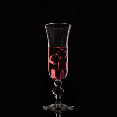 Pink drink in elegant glass with ice cubes backlit on black background