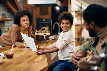 Happy black boy holding music sheet while his father is playing acoustic guitar at home.